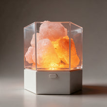 Modern Himalayan salt lamp lit in its steady orange mode, rough salt chunks inside the clear hexagonal case on a white base