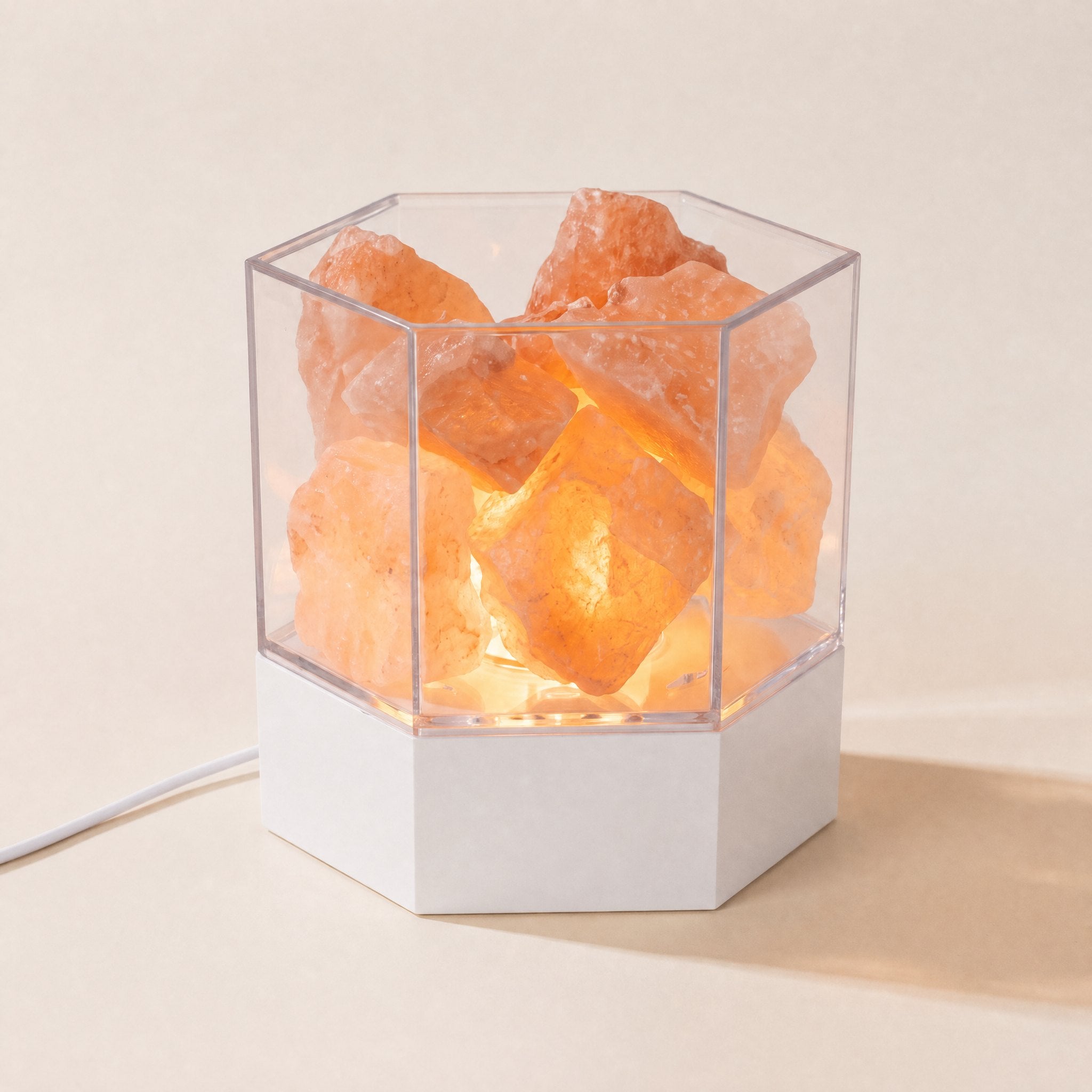Modern Himalayan salt lamp with real pink salt chunks glowing in a clear hexagonal case on a white base