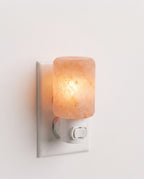 Himalayan salt crystal wall lamp plugged into a white outlet, glowing warm amber