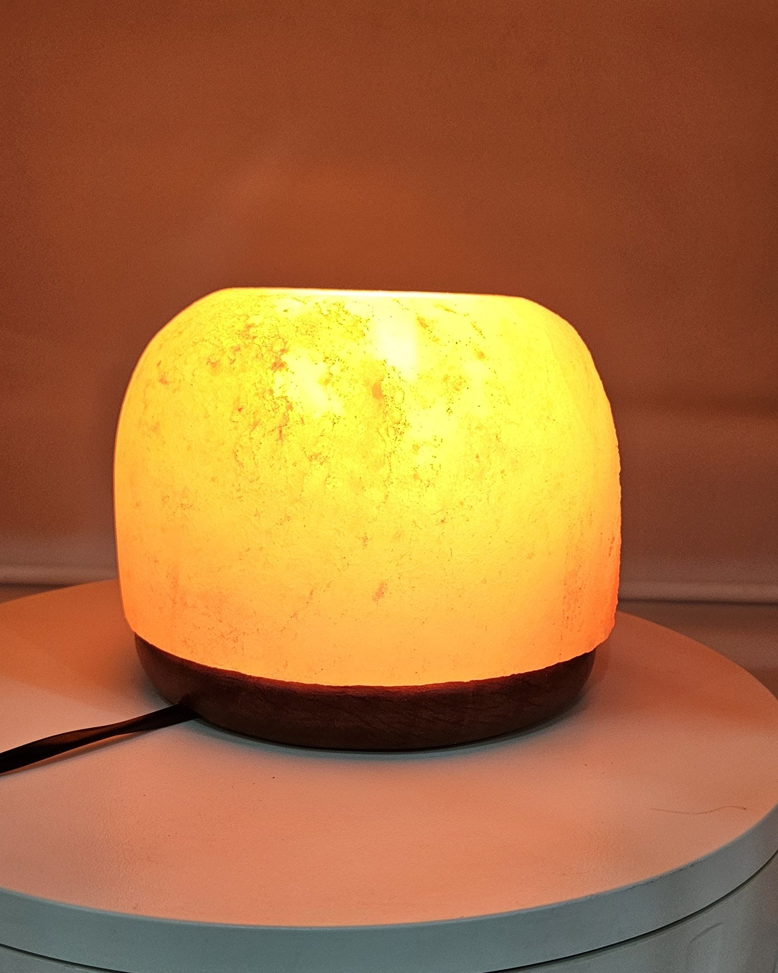 Himalayan salt dome lamp lit, on a turned base with the power cord visible
