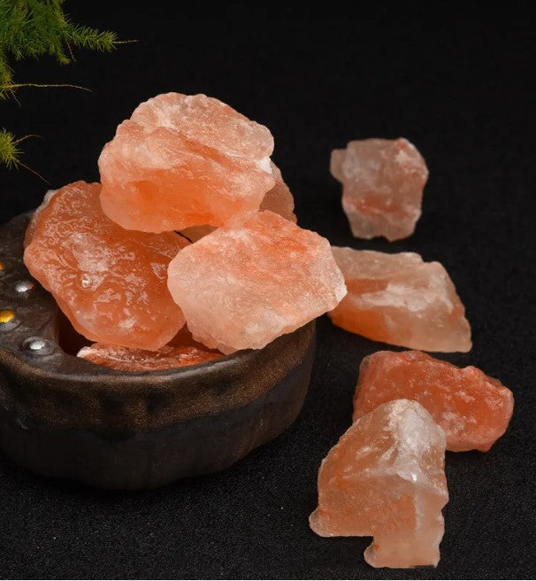 Rough orange salt stones in a dark ceramic dish with loose pieces alongside