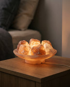 Himalayan salt rocks topping up a salt lamp dish glowing warm amber, power cord visible