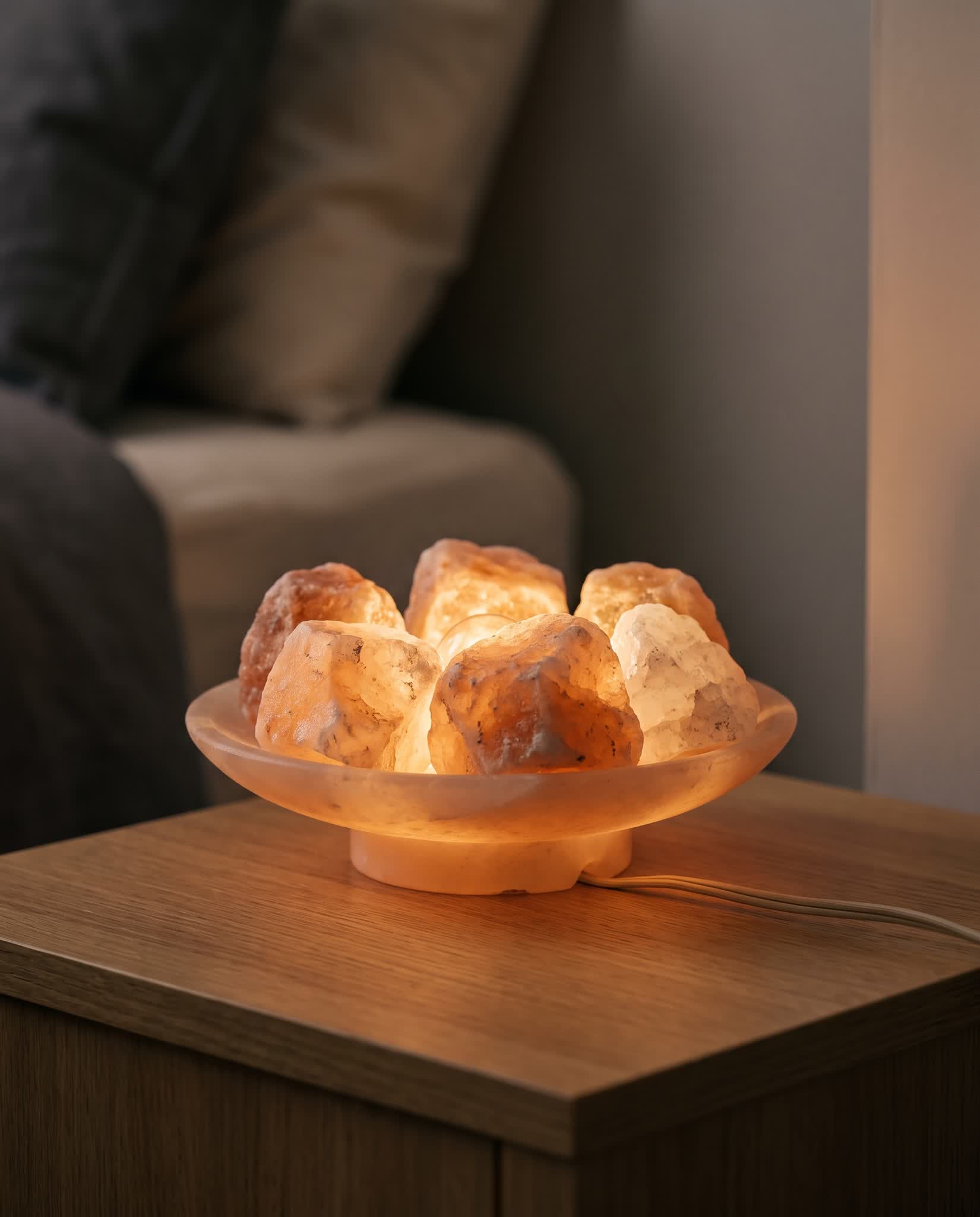 Himalayan salt rocks topping up a salt lamp dish glowing warm amber, power cord visible