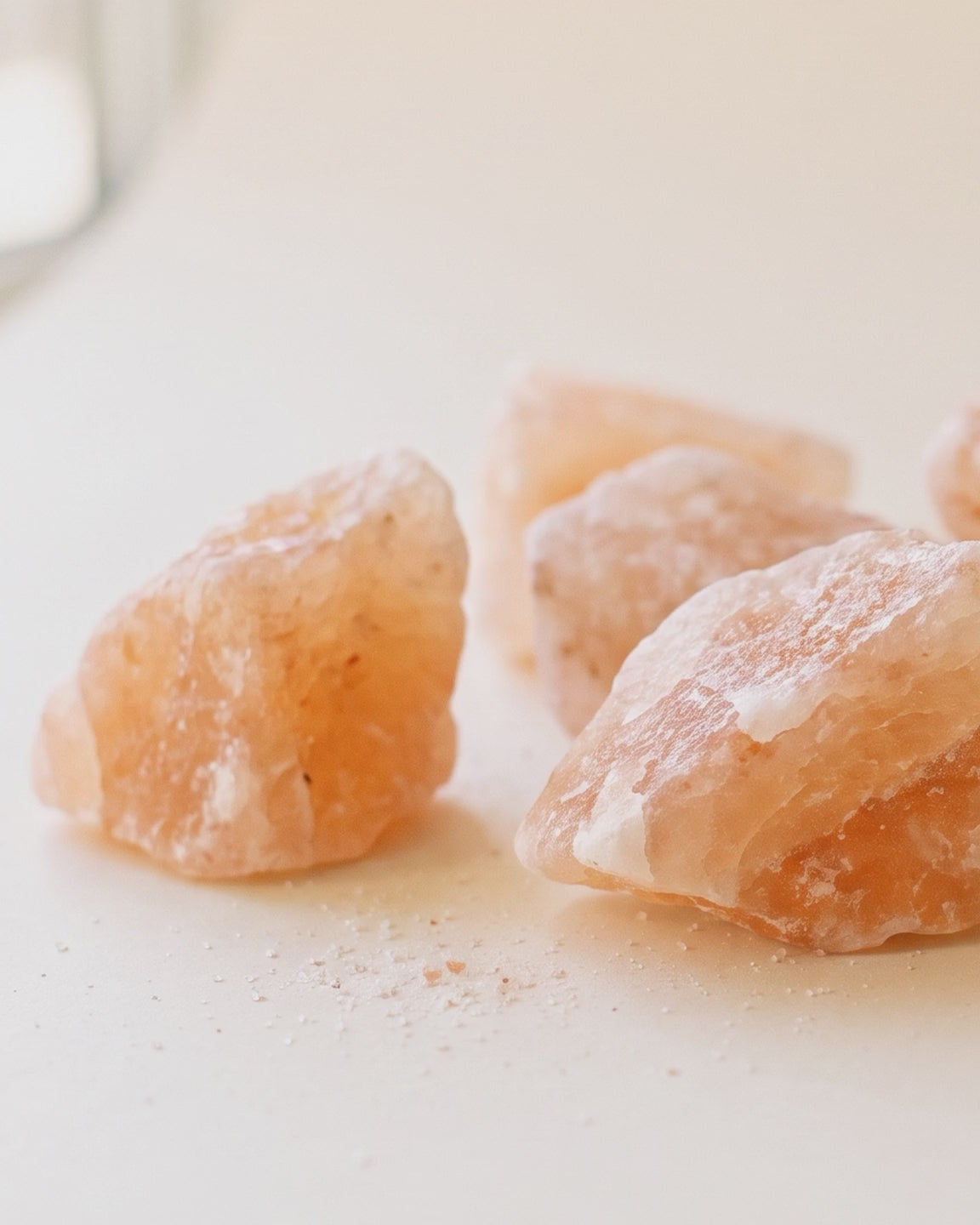 Rough uncarved Himalayan salt rocks on a pale surface, slow pan across the natural crystal texture