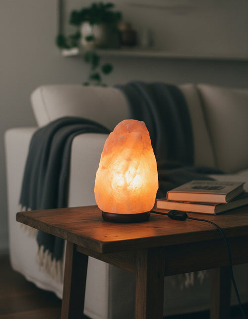 Natural Himalayan pink salt lamp with wood base glowing warm on a living room side table, power cord and inline switch visible