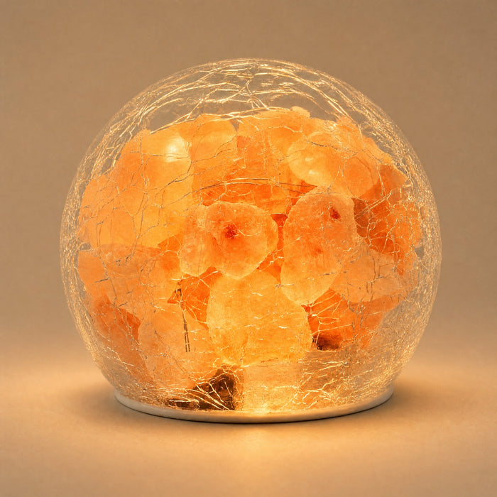 Battery powered mini Himalayan salt lamp switched on, rough pink salt pieces glowing warm amber inside a clear crackle-finish glass globe on a small white base