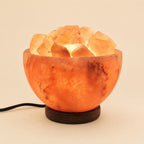 Himalayan salt bowl lamp filled with lit salt chunks on a dark wooden base, power cord visible
