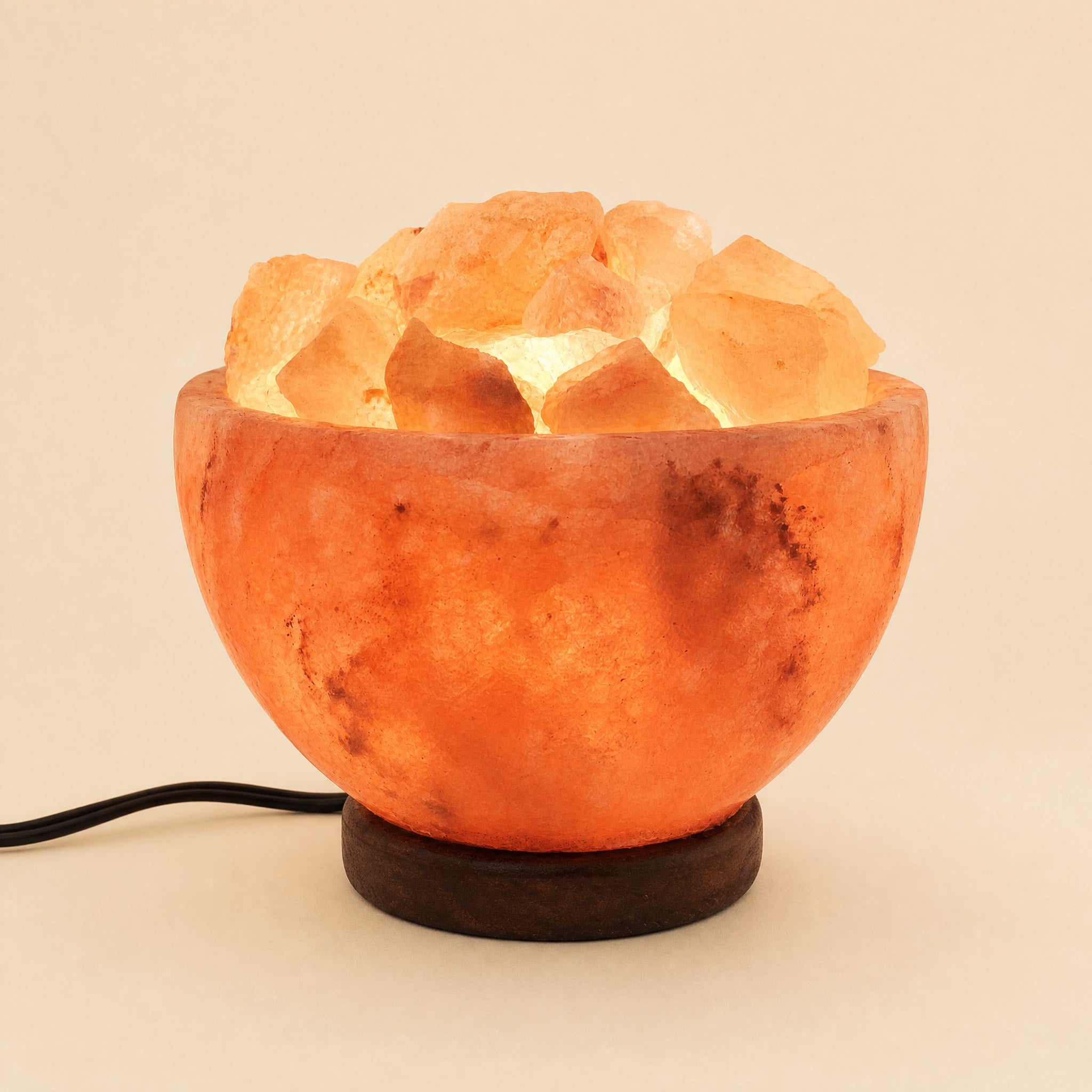 Himalayan salt bowl lamp filled with lit salt chunks on a dark wooden base, power cord visible