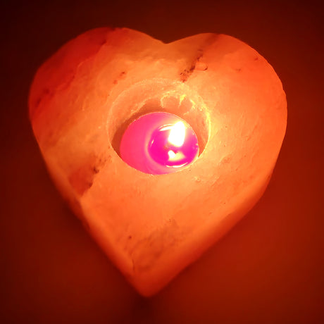 Heart Himalayan salt tea light holder with a central well, a tea light burning in it, the whole heart lit through