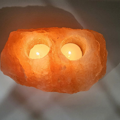 Natural Himalayan salt tea light holder with two wells, both tea lights burning, the whole stone glowing
