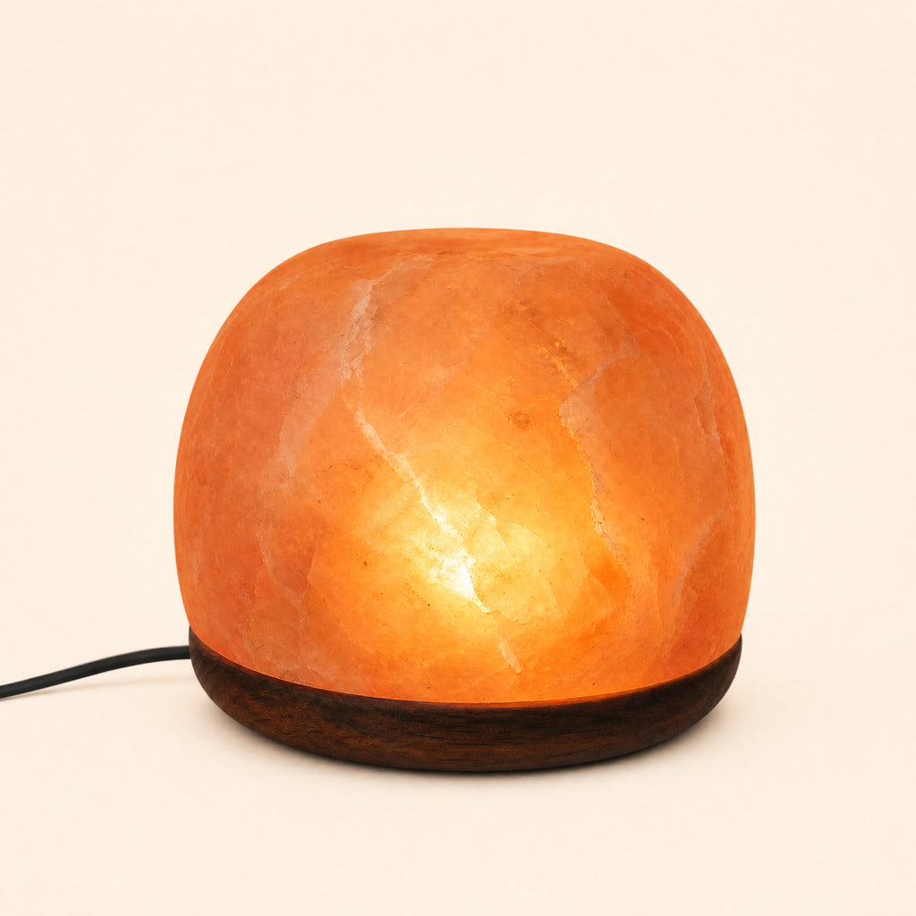 Dome Himalayan salt lamp lit on a dark wooden base, power cord visible