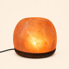 Dome Himalayan salt lamp lit on a dark wooden base, power cord visible
