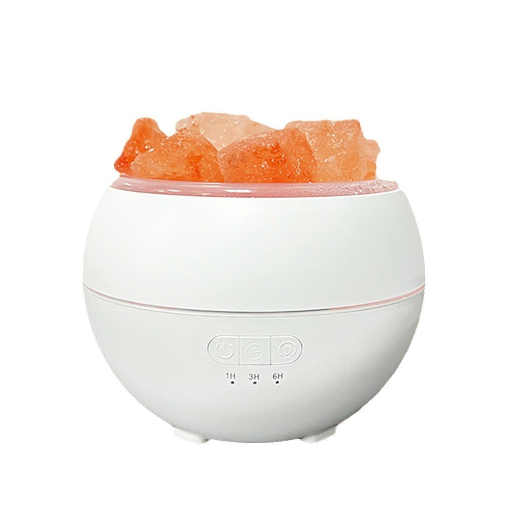 Mini salt humidifier unlit on a white background: white sphere with a ring of rough pink Himalayan salt pieces around the top opening