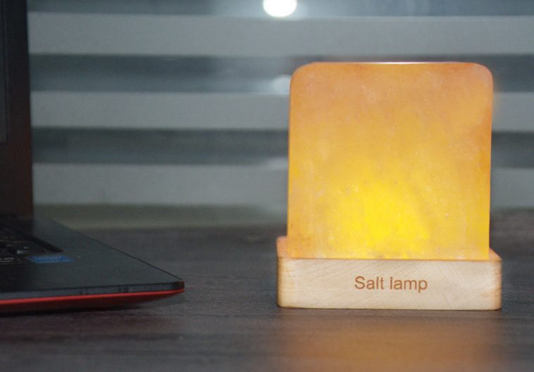 A hand-carved Himalayan salt lamp glowing on a solid wooden base