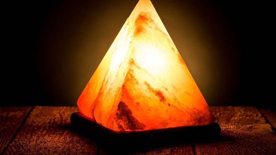 A solid hand-carved Himalayan salt lamp glowing on a wooden base