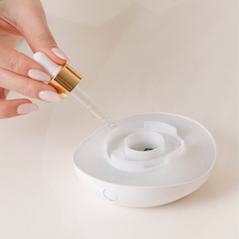 A dropper adding essential oil to the ring in the unplugged lamp base, salt cup lifted off